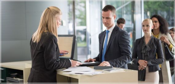 A man gets assistance at bank counter while others wait in line behind him. 