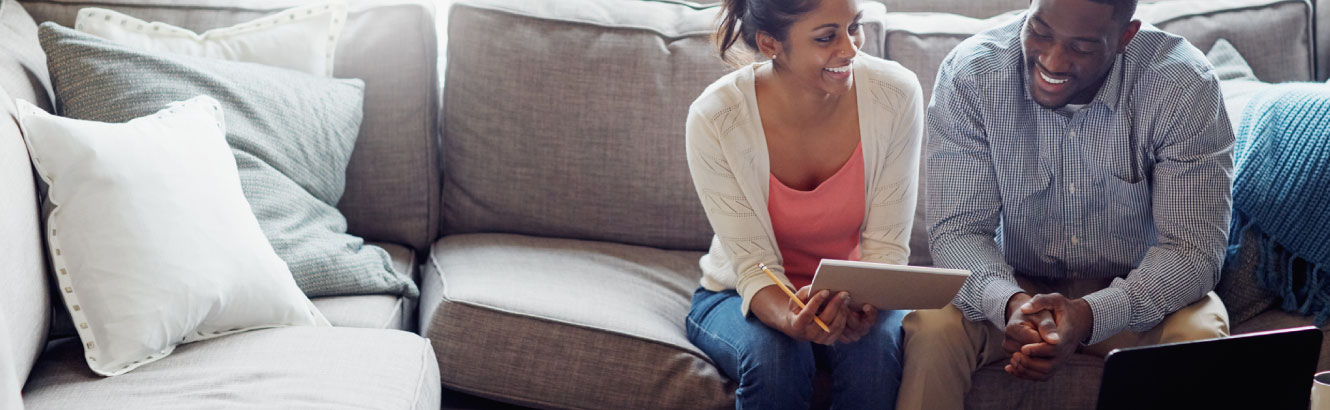 Young couple sitting on their couch with computer sitting in front of them.